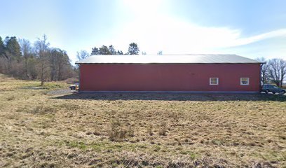 Röd lagerbyggnad i enkel stil på öppen mark med skog i bakgrunden och två parkerade bilar.