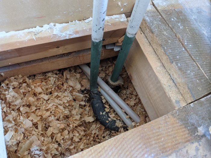 17 mm järnrör för vattenburen värme och PVC-rör på ett trägolv täckt med sågspån.
