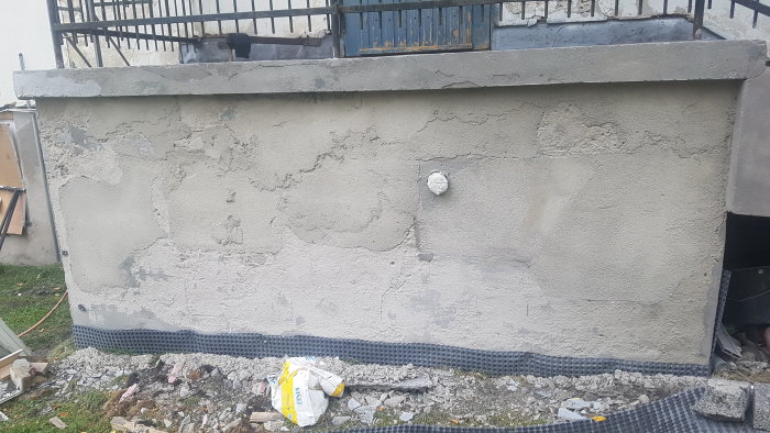 Delvis blästrad vägg med synliga skador och avlägsnad nedre färg, med renoveringsavfall framför.