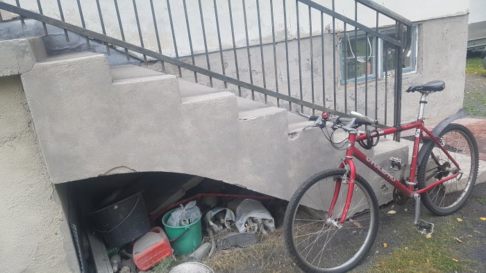 Betongtrappa med blästrat område och skador nedtill, rött cykeln står lutad mot räcket.