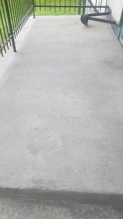 En blästrad betongplatta på en balkong med synliga skador och en metallskena längs kanten.