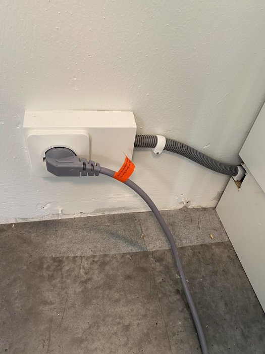 Vägguttag med ansluten elkabel och kabelskydd som ordnats snyggt längs med väggen.