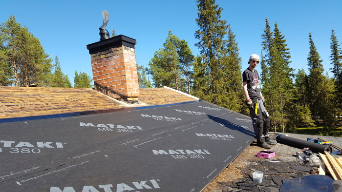 Person arbetar med takbyte, med verktyg och material synligt på det halvrivna taket.