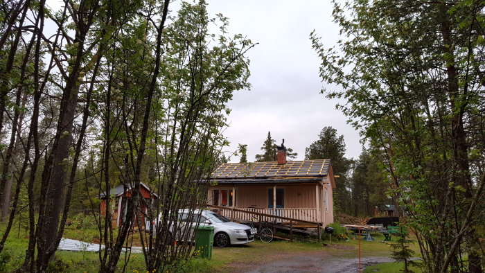 Hus med delvis färdiglagt tak och synliga läktbrädor, omgivet av grön skog, i regnigt väder.