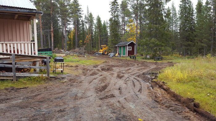 Muddy construction site with heavy machinery, upturned soil, and forest in the background.