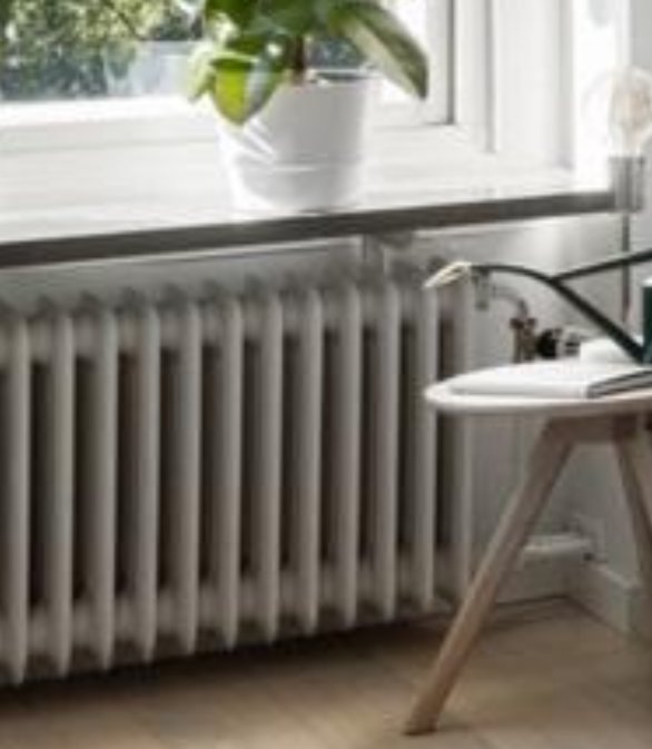 Gammal stil radiator under ett fönster i rum med växt och bord.