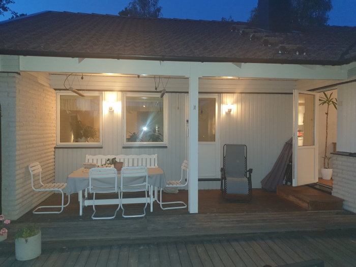Altan med utemöbler och en synlig stolpe under taket som bär upp en limträbalk, med öppna terrassdörrar in till huset.