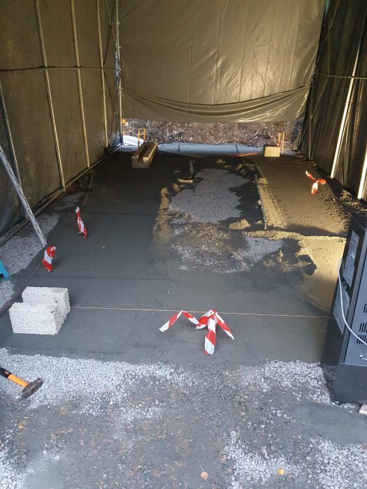 Nygrundad källare i byggtält med betonggolv, grussäng och byggmaterial.
