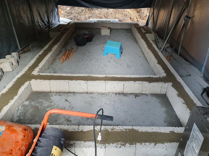 Grundläggning av jordkällare under konstruktionstält med betongblock och isolering.