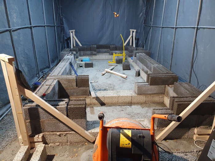 Grundkonstruktion av jordkällare med betongblock inuti ett tältbygge.