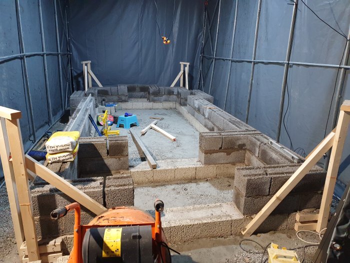 Byggarbetsplats för källarbygge med grund av betongblock inne i tält med verktyg och byggmaterial.