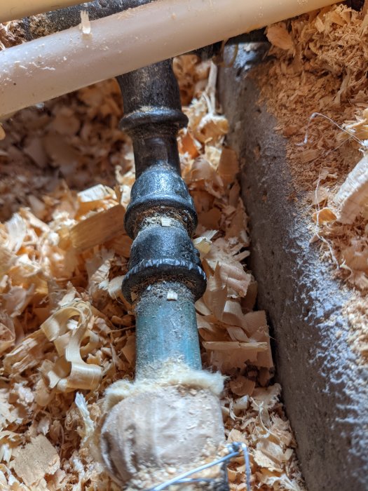 Ett avkapat rör omgivet av träspån i ett pågående VVS-arbete.