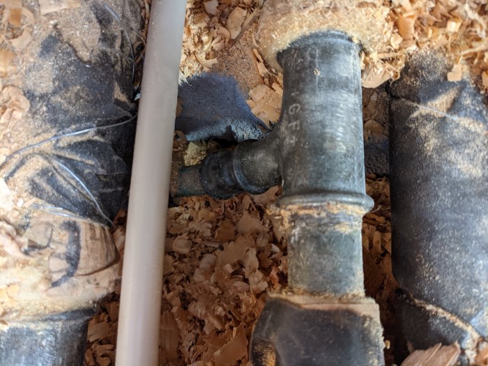 Ett avklippt rör och en rörförgrening visas, omgivna av sågspån, i ett under arbete pågående VVS-projekt.