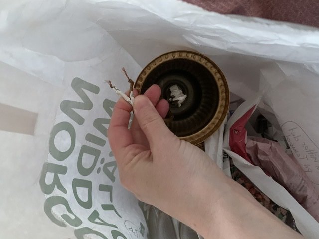 Hand håller en äldre taklampa med oskyddade elektriska ledningar mot en IKEA-påse.