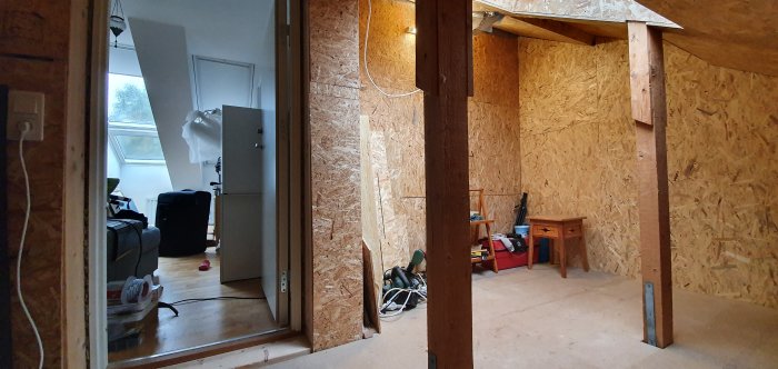 Ett rum under renovering med OSB-paneler på väggarna, oavslutade delar och byggmaterial synliga.