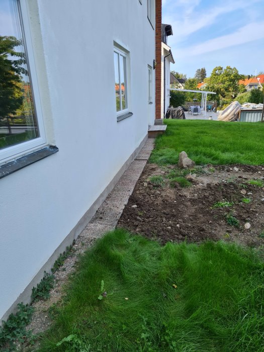 Nygrävd mark och återlagda stenar längs husfasad efter servicearbete.