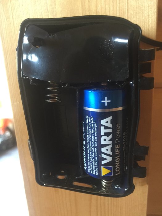 Deformerad batterilåda med en blå och gul VARTA batteri monterad i en LED-belysningsenhet.