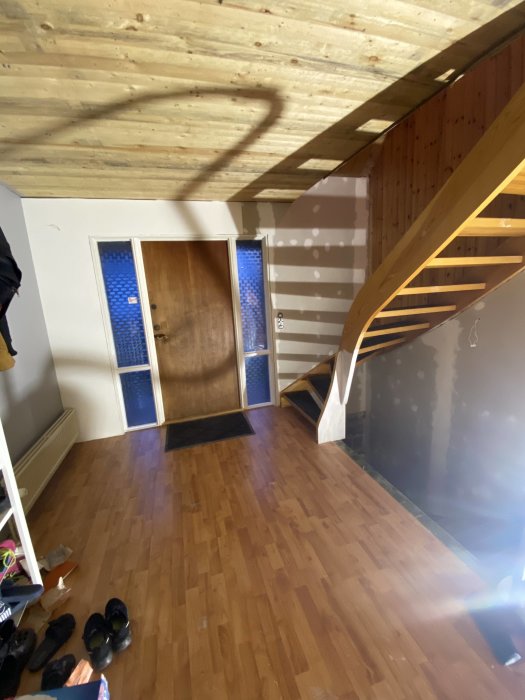 Hall med påbörjad tapetsering, trätrappa och parkettgolv.