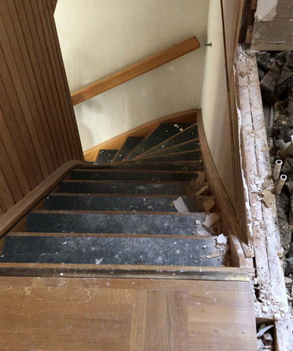 Delvis raserad trätrappa inomhus med byggavfall, fotograferad uppifrån.