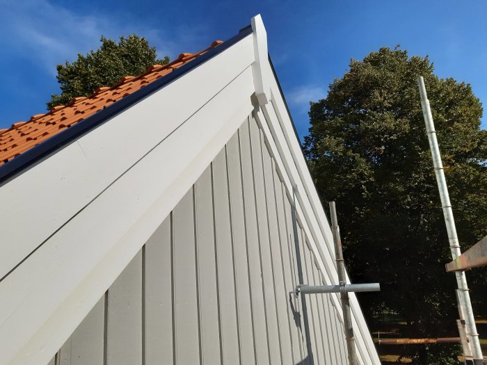 Renoverat hus med nymålade vindskivor och vattbrädor mot en klarblå himmel.