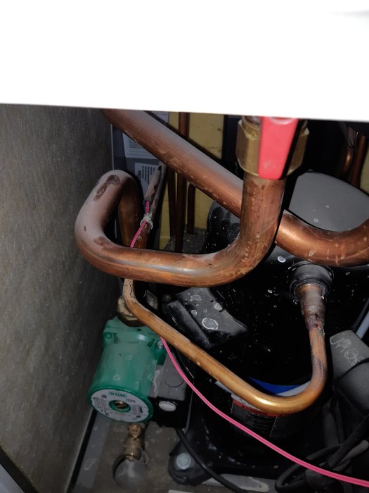 Värmepumpsinstallation med synlig skadad och otäckt kabel bredvid kopparledningar.
