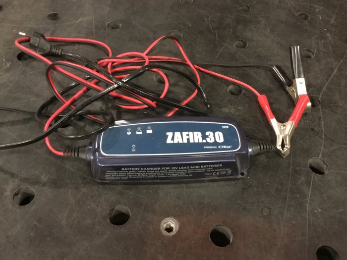 Batteriladdare märkt ZAFIR 3.0 med klämmor och intrasslade kablar på en svart perforerad yta.