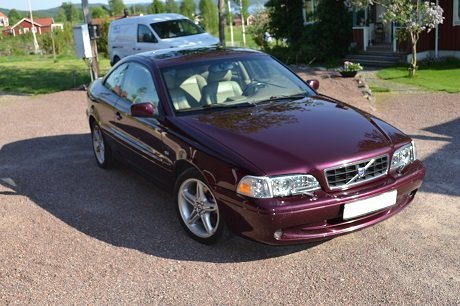 Lila Volvo C70 Coupe T5 från 1998 parkerad på en grusuppfart med grönska i bakgrunden.