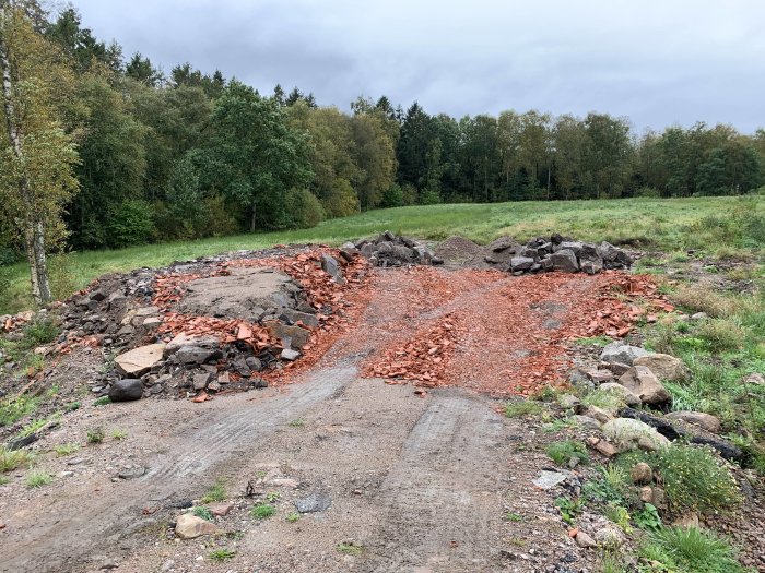 Grusväg med högar av krossade tegelstenar och stenblock på en byggarbetsplats.