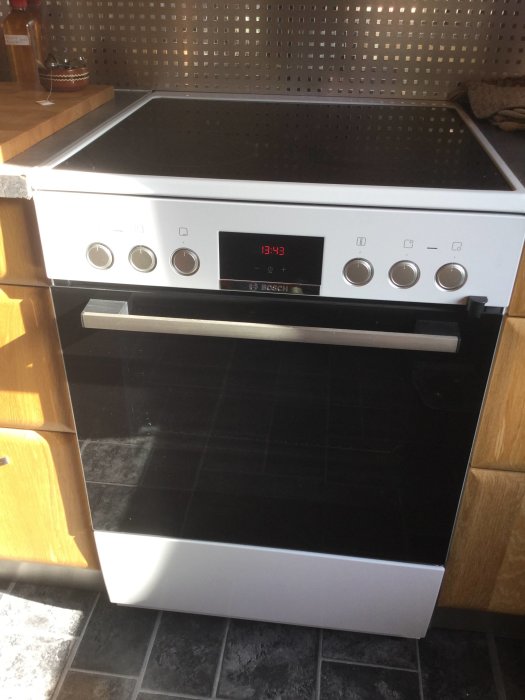 Nyinstallerad vit 400V spis i kök med digital klocka som visar 13:43, bredvid träskåp.
