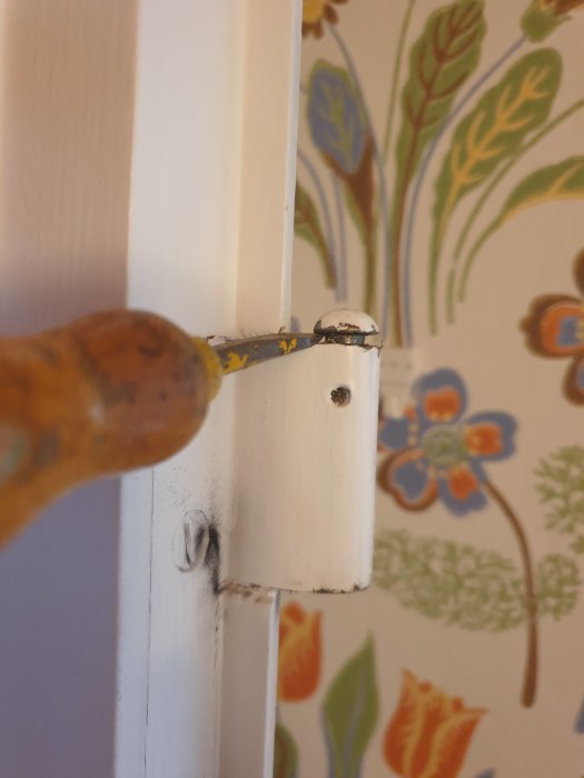 En hand håller en stämjärn mot en dörrkarm för att knacka ut en sprint från gångjärnet.