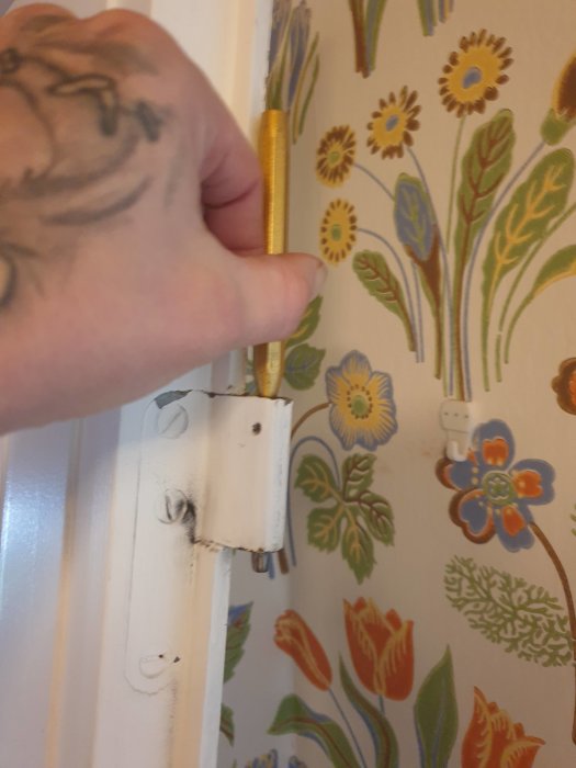 Närbild på en hand som knackar ur en sprint från dörrfäste mot blommigt tapetserad vägg.