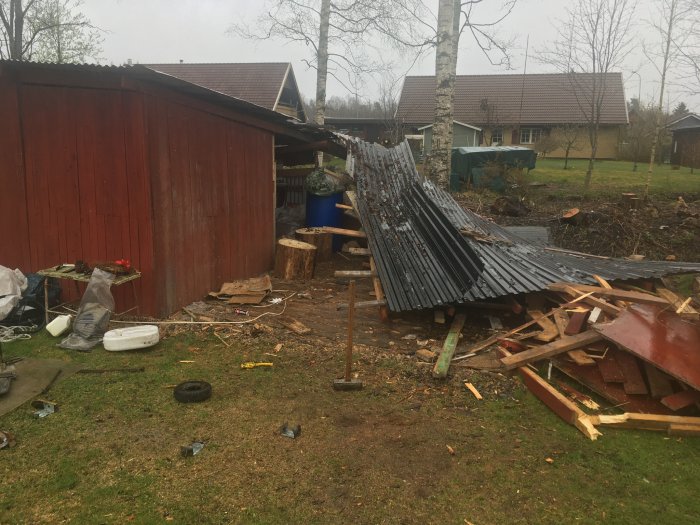 Rivet skjul med spiltor och brädor överallt, skadat tak ligger buckligt på marken.