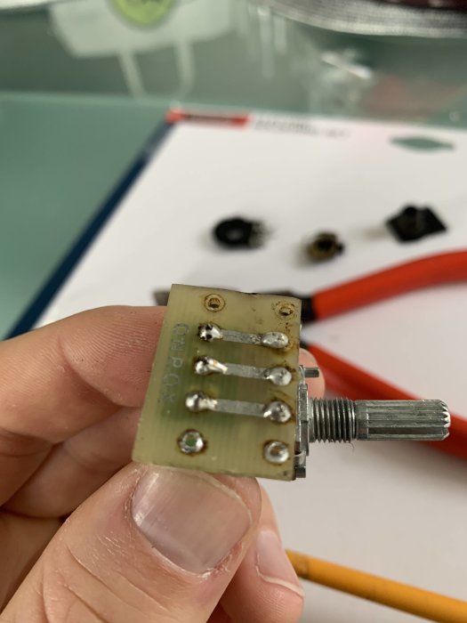 Hand håller en nylodad elektronisk komponent med lödpunkter framför suddig bakgrund med elektriska delar.