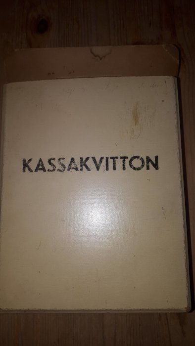 En förvaringslåda märkt med "KASSAKVITTON" på ett slitet trägolv.