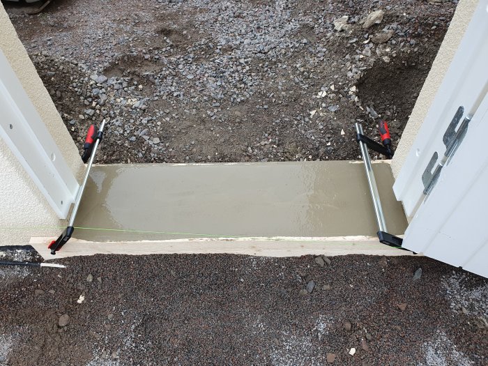 Nygjutet fundament för postlåda och tröskel mellan sjösten och gatsten vid en mur.