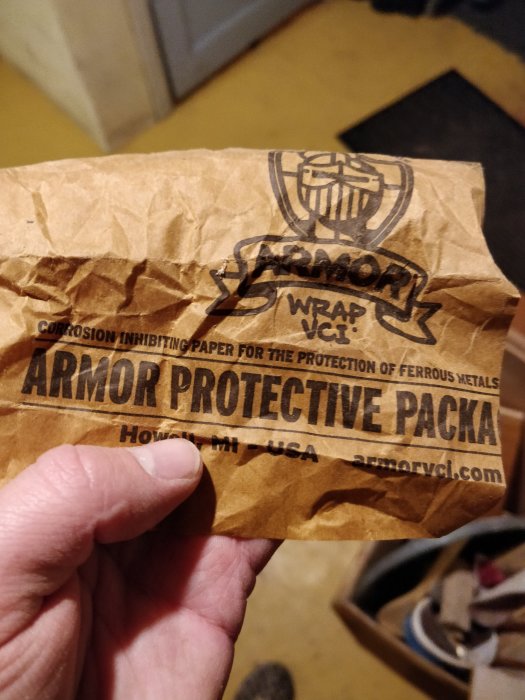 Hand som håller ett stycke brunt korrosionshämmande papper märkt "Armor Protective Packa".