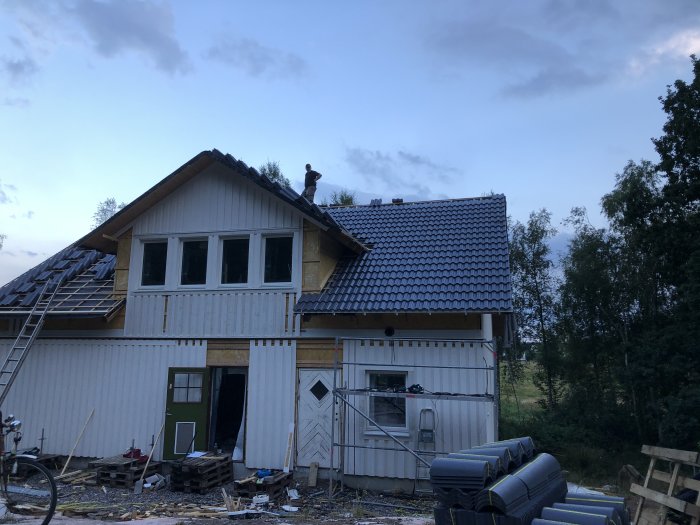 Person som arbetar på taket av ett hus under konstruktion med trävirke och byggmaterial i förgrunden.