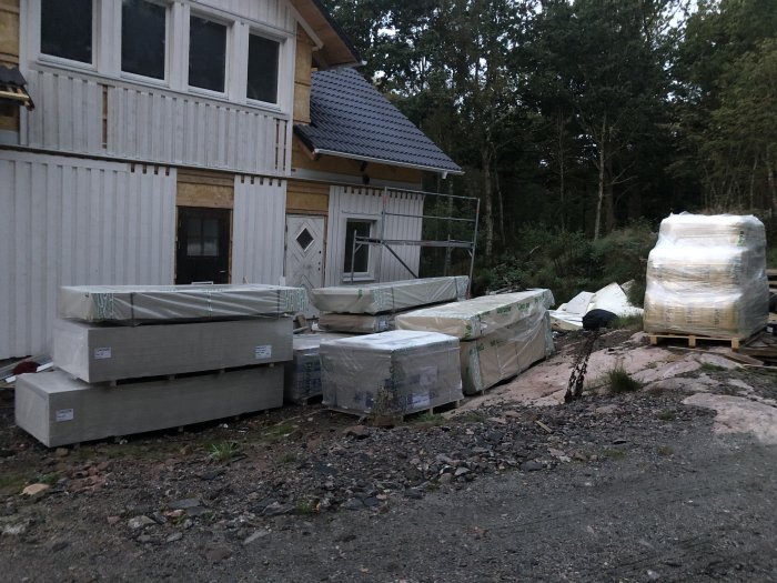 Obyggt hus med delvis pålagt tak, och byggmaterial som OSB och gipsskivor packat i högar framför.