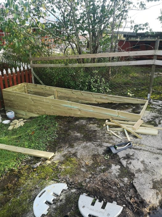 Halvfärdig, figursydd odlingslåda i trä under uppbyggnad utomhus med verktyg runtomkring.