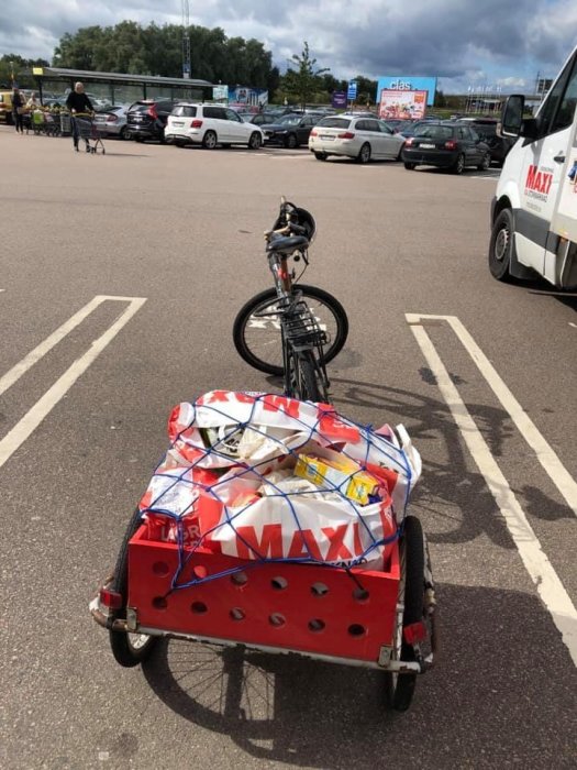 Cykel med cykelkärra lastad med flera plastpåsar säkrade med spännband på parkeringsplats.