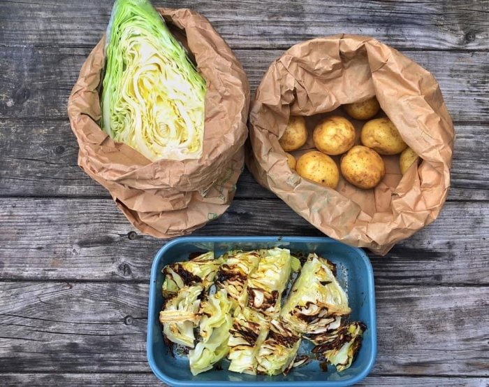 Två papperskassar med kålhuvud och potatis på träbord bredvid tillagad kål i en form.
