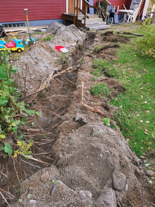 Nygrävd grävning för fiberinstallation med synliga rötter och uppbruten asfalt nära hus och leksaker.