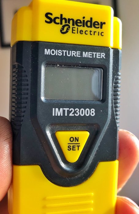 En hand håller en fuktmätare av märket Schneider Electric modell IMT23008.