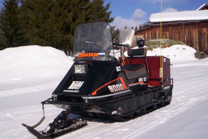 Svart röd bandvagn på snötäckt mark med skyltar som liknar grävmaskin.