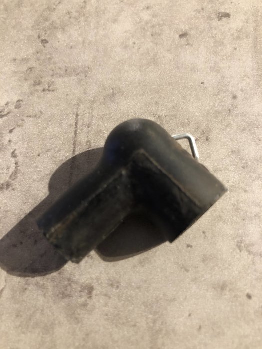 Svart hatt av gummi med synlig fjäder inuti som ligger på en grå yta.