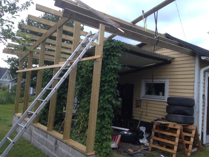 Byggprojekt av en carport/grillplats bredvid ett garage, obehandlad träkonstruktion och murade lecablock.