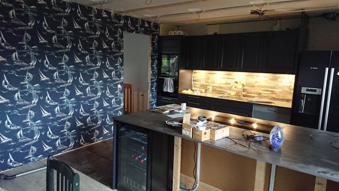 Ett ombyggt kök med nymålad mönstrad vägg med segelbåtar, mörka skåp och belysning under överskåpen.
