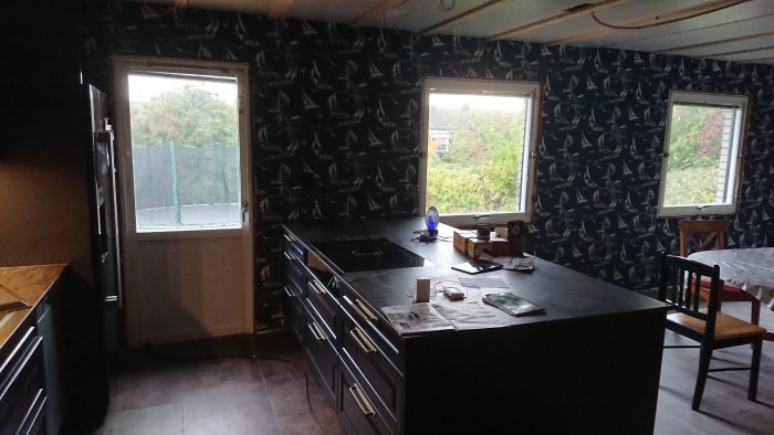 Kök med nymålade mörka väggar och tapet, svarta skåp och ett köksbord.