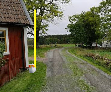 En grusväg bredvid ett hus med en gul linje som visar den föreslagna tomtgränsen, med en gränssten vid linjens början.