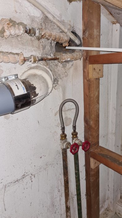 Renoveringsarbete med synliga rör och armering i en vägg, inklusive avstängda varm- och kallvattenledningar.
